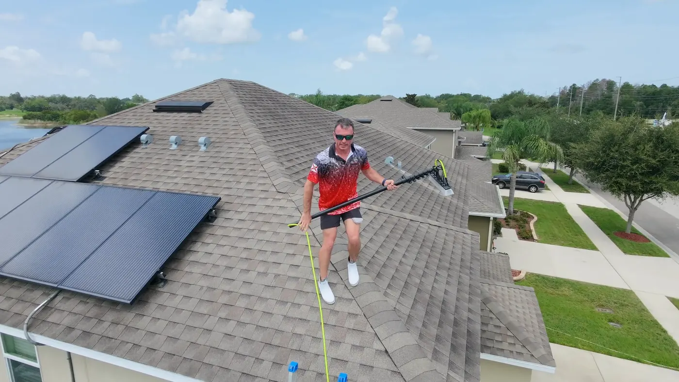 Iron Shield technician working along a roof beside a residential solar array, hose in hand