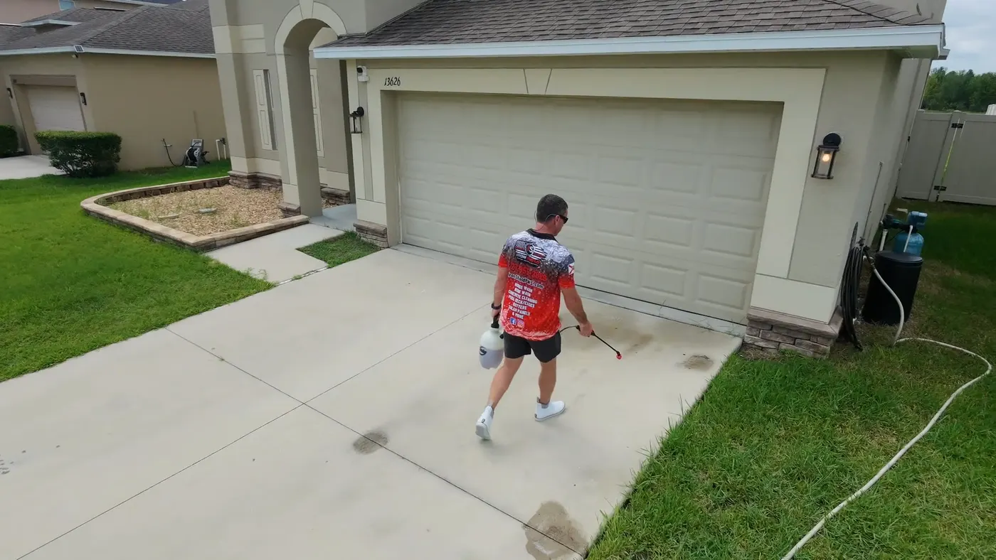 Iron Shield technician spraying cleaning solution onto stained concrete directly in front of a garage door