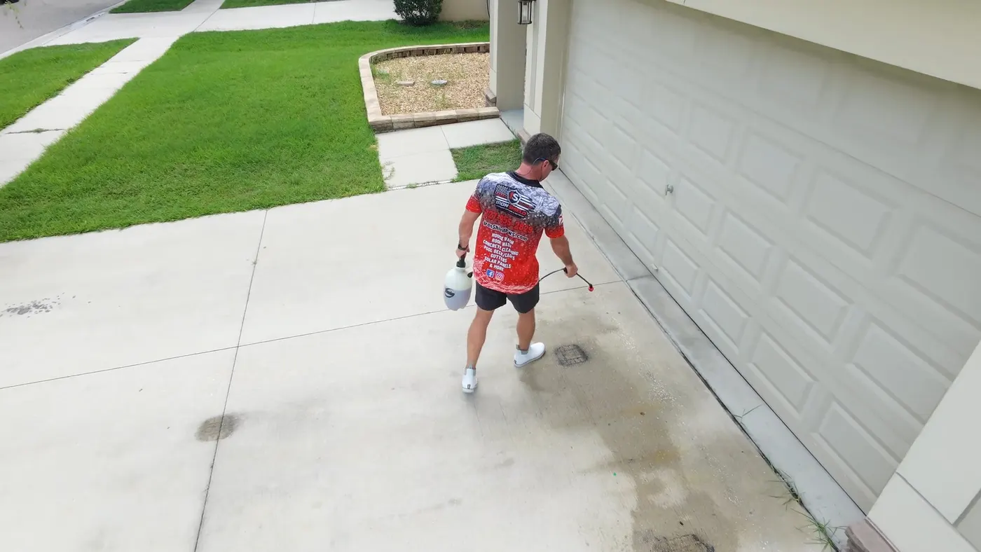 Iron Shield technician working down a concrete driveway, applying cleaning solution to the darker, stained sections