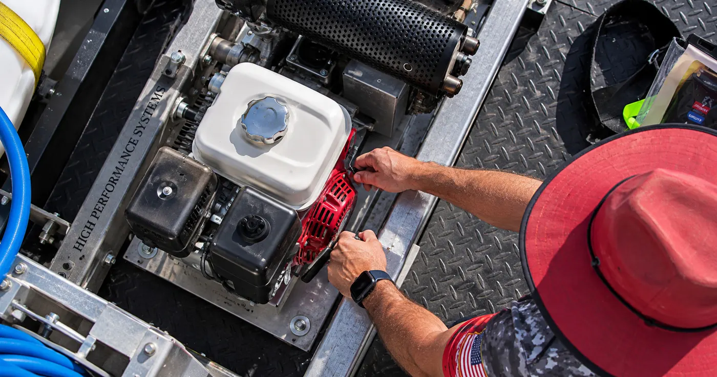 Close-up of an Iron Shield technician starting the pressure washer engine mounted on the service trailer