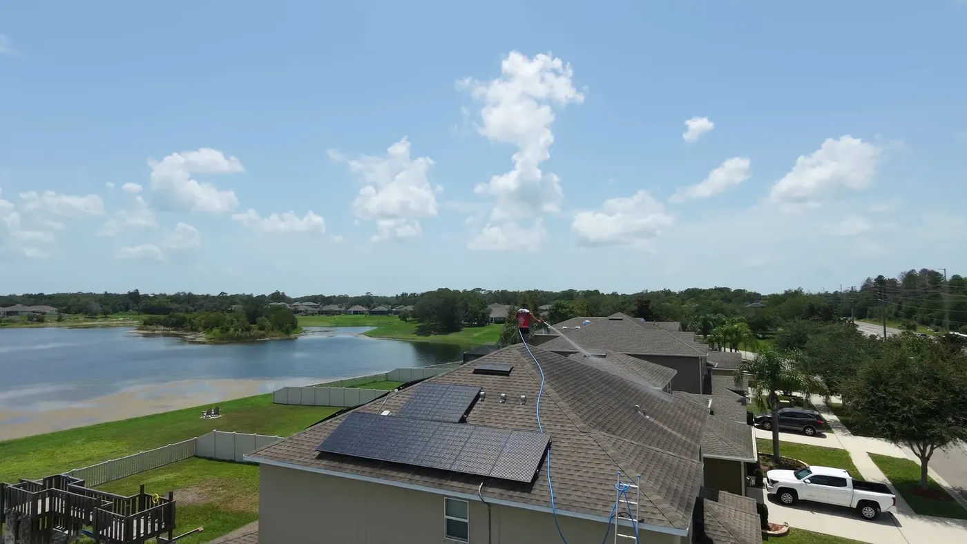 Wide aerial view of a lakeside community home with an Iron Shield technician working across its roof