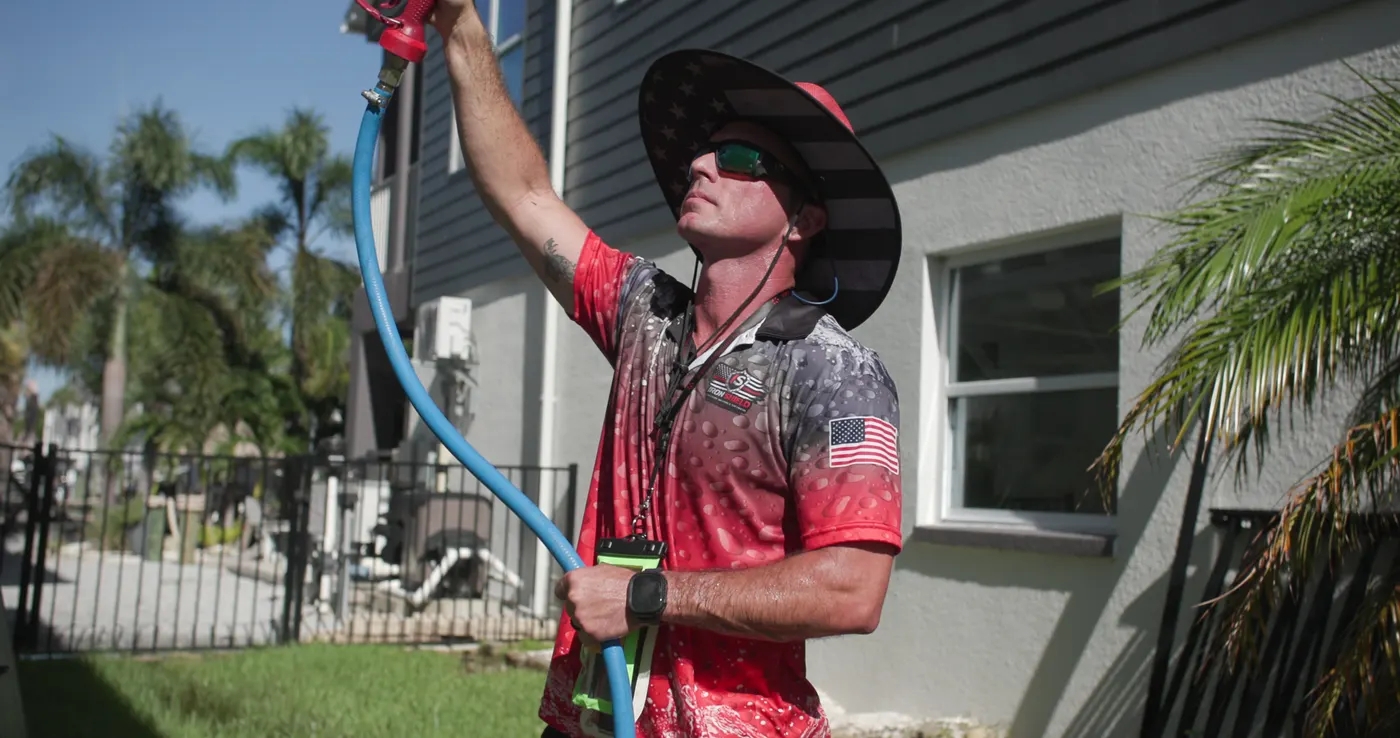 Close view of an Iron Shield technician directing the cleaning solution at the elevated sections of a home exterior