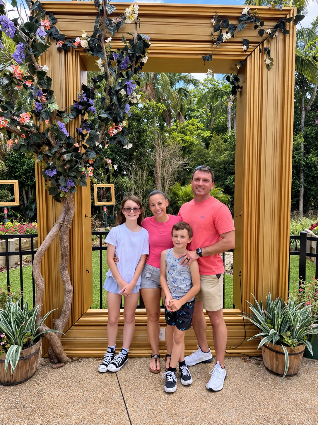 The family behind Iron Shield standing together inside a tall gold picture frame decorated with flowers and foliage, in a garden