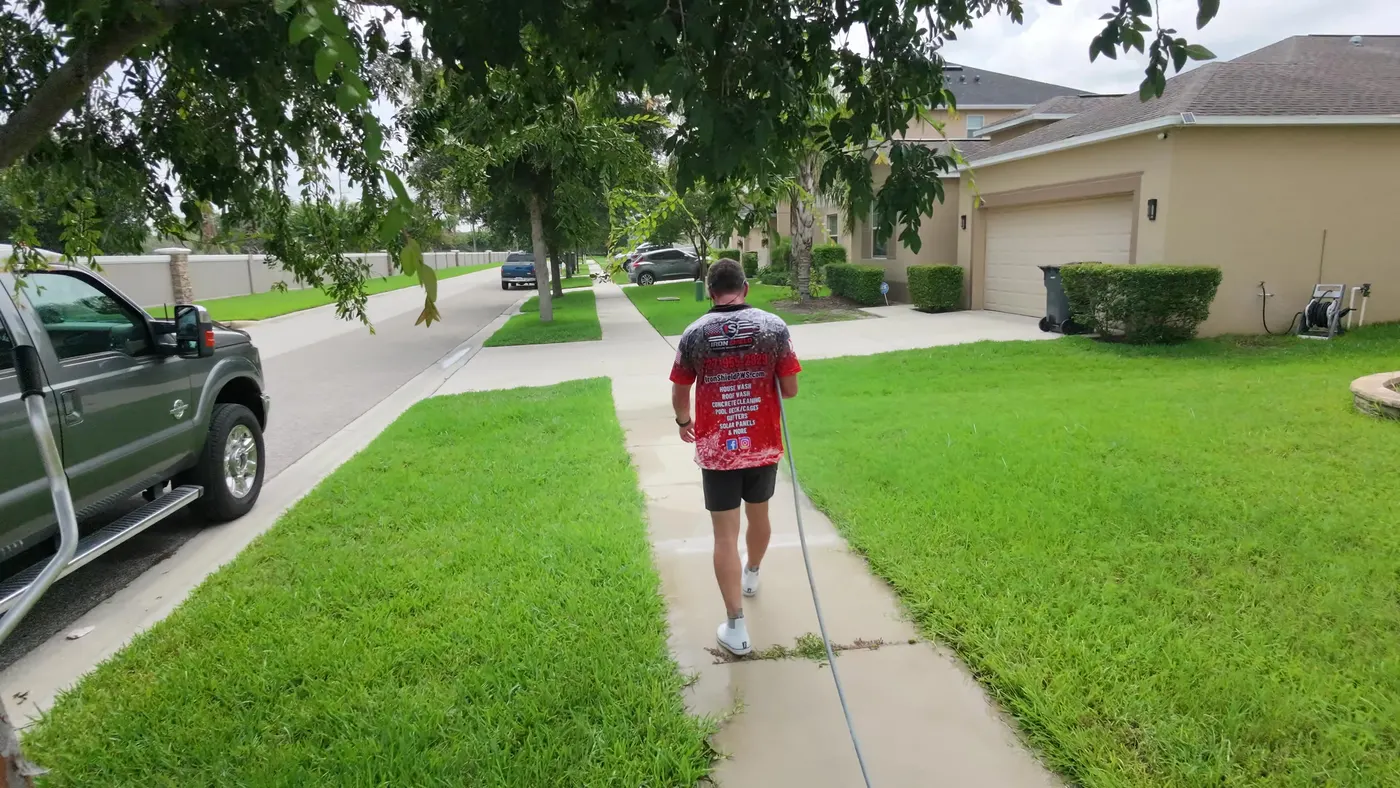 Iron Shield technician walking a long residential sidewalk with the hose line, lawns and homes on either side